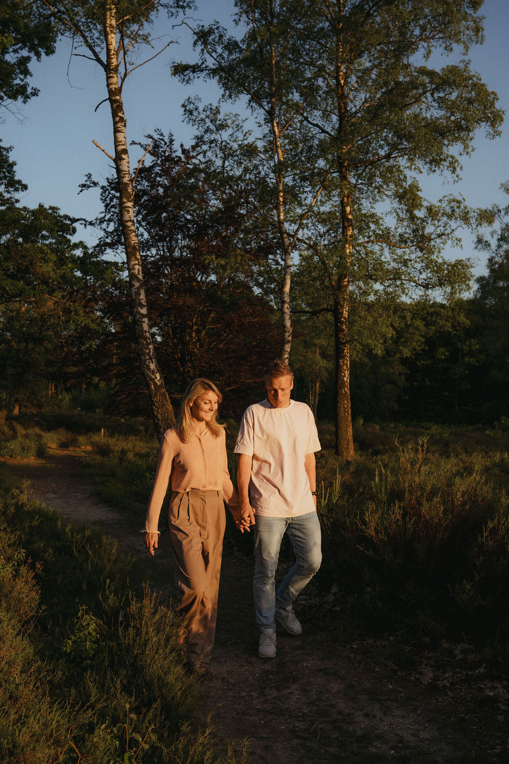 Margo en Joris, relatiecoaches van het Atelier voor Liefde in Maarn (regio Utrecht), lopen hand in hand over een zandpad door bos en heide in het avondlicht